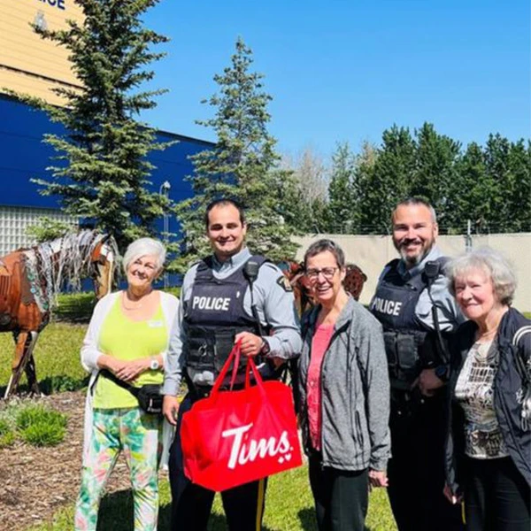 Three seniors taking a photo with two police officers. The one policeman is holding a bag of Tim Horton's doughnuts.