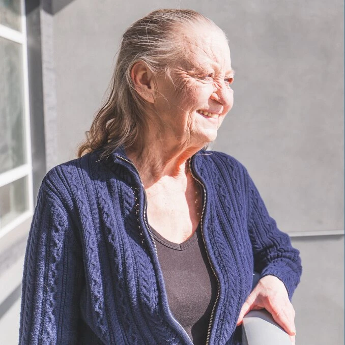 An elderly lady smiling and standing at balcony